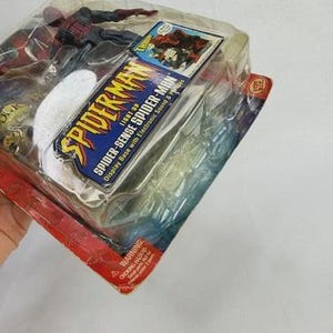 Peut inclure: Une figurine de Spider-Man dans un emballage en plastique. L'emballage comprend le texte "Spider-Man" et "Spider-Sense Spider-Man". La figurine est rouge et noire. L'emballage a une palette de couleurs rouge et bleu.