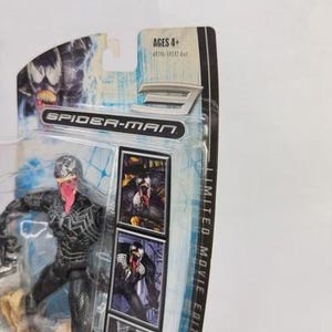 May include: A Spider-Man action figure of Venom, a black and white character with a pink tongue, in a plastic package. The package includes the text "Spider-Man" and "Limited Movie Edition". The age range is Ages 4+.
