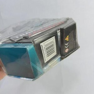 Puede incluir: Un producto empaquetado con una caja negra y turquesa, envuelto en pl&aacute;stico transparente. La caja tiene un c&oacute;digo de barras y texto. El producto es parcialmente visible, con texto rojo y blanco en la parte superior.