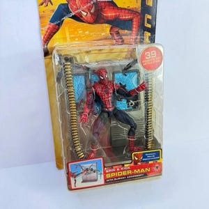 May include: Spider-Man action figure in a clear plastic package. The figure is red and black, with multiple points of articulation. The packaging includes the text "SPIN & KICK SPIDER-MAN WITH SUBWAY ACCESSORY" and "39 POINTS OF ARTICULATION".