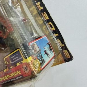 May include: Sealed Spider-Man toy package. The packaging is red and gold with the words "Spider-Man" and "Official Movie Merchandise." A small image shows Spider-Man swinging. The package includes a magnetic projectile launcher.