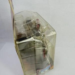 May include: A packaged action figure, encased in clear plastic. The figure appears to be a character from a movie or television show, with a detailed design. The packaging includes a cardboard backing with printed graphics and text.