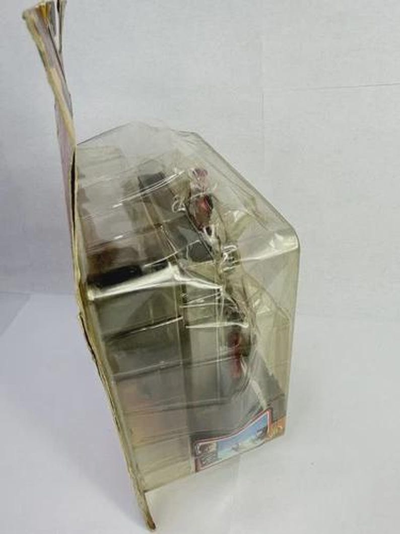 May include: A packaged action figure, encased in clear plastic. The figure appears to be a character from a movie or television show, with a detailed design. The packaging includes a cardboard backing with printed graphics and text.