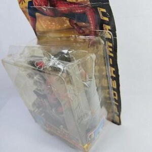 May include: A Spider-Man action figure in its original packaging. The packaging features a red and black Spider-Man graphic. The figure is visible through a clear plastic casing. The packaging also includes the text "Spider-Man".