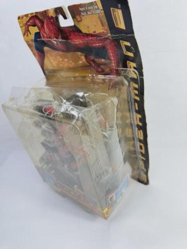 May include: A Spider-Man action figure in its original packaging. The packaging features a red and black Spider-Man graphic. The figure is visible through a clear plastic casing. The packaging also includes the text "Spider-Man".