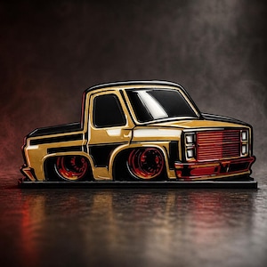May include: A stylized gold and black pickup truck with red accents. The truck features a lowered suspension and custom wheels. The front grille and wheels are red. The truck is set against a dark, smoky background.