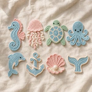 Könnte beinhalten: Ein Set aus acht gehäkelten Applikationen mit Ozeanmotiven, bestehend aus einem hellblauen Seepferdchen, einer rosa Qualle, einer grünen Meeresschildkröte, einem hellblauen Oktopus, einem hellblauen Delfin, einem hellblauen Anker, einer rosa Muschel und einer Walflosse.