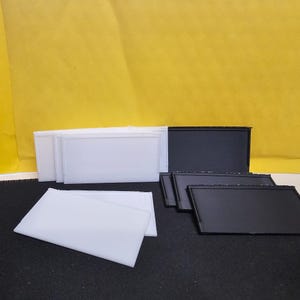 Può includere: Una collezione di pannelli rettangolari bianchi e neri. I pannelli bianchi sono impilati e disposti in fila, mentre i pannelli neri sono raggruppati. Lo sfondo è giallo brillante.