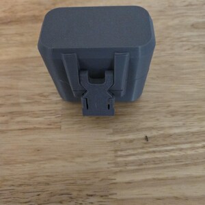 Op de afbeelding: Een donkergrijze rechthoekige opbergdoos met afgeronde hoeken en een getextureerde matte afwerking. De doos is voorzien van een centraal verticaal sluitmechanisme aan de voorzijde om het deksel aan de basis van de unit te bevestigen.