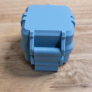 May include: A light blue, square-shaped, 3D-printed storage container with a hinged lid and a latch mechanism on the front. The text 'Digital Download' is printed in black above the object, which features visible horizontal layer lines.