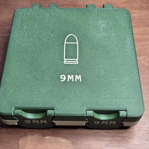 May include: A green rectangular case with a white outline of a bullet and the text "9 MM" printed on the top. The case has two clasps and the text "9 MM" printed on the clasps.