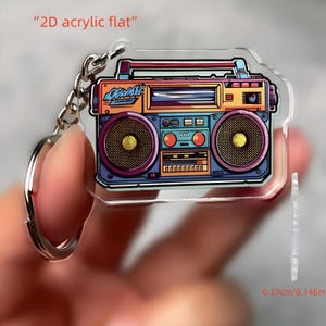 May include: A clear acrylic keychain featuring a colorful, retro boombox design. The boombox has orange, purple, blue, and yellow accents. The keychain is 0.146 inches thick and includes a silver keyring.