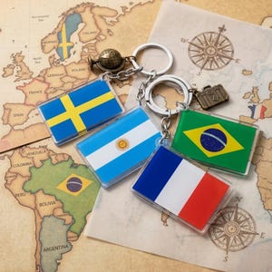May include: Keychains featuring flags of Sweden, Argentina, Brazil, and France. Each keychain has a clear acrylic flag design with a metal keyring. The background includes a vintage map and compass rose.