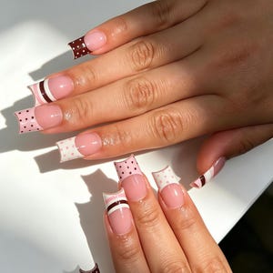 May include: Square-shaped artificial nails featuring a French manicure style with a nude base. The tips alternate between dark brown with white polka dots, light pink with dark brown polka dots, and a layered design of brown, white, and pink stripes.