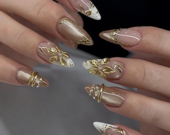 Unghie finte di lusso con foglia d'oro e fiore 3D, base a occhio di gatto beige metallizzato, unghie finte extra lunghe e appuntite, eleganti punte bianche.