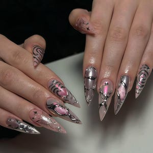 Puede incluir: Uñas largas y puntiagudas con una base rosa claro. Cada uña presenta diseños intrincados, que incluyen detalles metálicos plateados, formas de corazón rosa y patrones arremolinados. Algunas uñas tienen pequeños detalles de estrellas y purpurina.