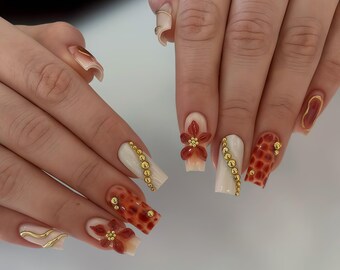 Unhas postiças personalizadas em padrão tartaruga, com flor vermelha 3D e miçangas douradas, formato quadrado, conjunto moderno e exclusivo.