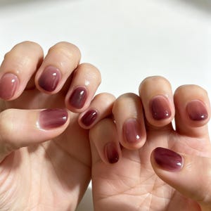 Peut inclure: Ongles courts et arrondis avec une finition dégradée brillante et semi-transparente. La couleur passe d'un prune ou bordeaux profond et foncé à la base de chaque ongle à une teinte mauve ou rose poudré plus claire et translucide vers les pointes.