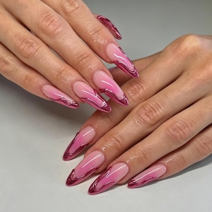 May include: Long almond-shaped nails featuring a soft pink gradient base color. Each nail is accented with a metallic magenta chrome swirl design that follows the curve of the nail tip, creating a reflective and dimensional liquid-like appearance.