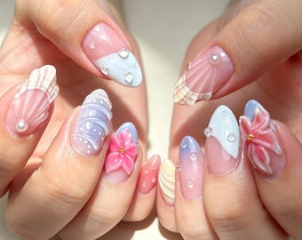 Unhas postiças em tons pastel de rosa e azul com conchas, formato amêndoa com flor 3D, pérola e gota d'água, acabamento nude brilhante, reutilizáveis e perfeitas para o verão na praia.