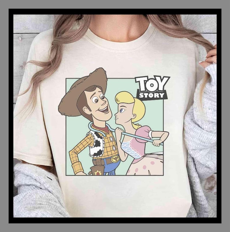 Puede incluir: Camiseta color crema con un gr&aacute;fico de dibujos animados de Woody y Bo Peep de Toy Story. Woody lleva un sombrero de vaquero y un chaleco, mientras que Bo Peep lleva un vestido rosa. Las palabras "TOY STORY" est&aacute;n impresas en negro sobre los personajes.