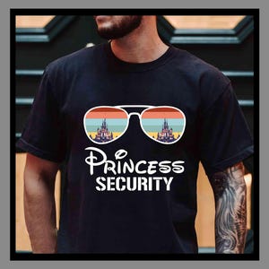 Może przedstawiać: Czarny t-shirt z białym nadrukiem. Grafika przedstawia okulary przeciwsłoneczne odbijające zachód słońca i zamek. Poniżej tekst "Princess Security". Styl retro.