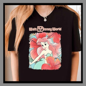 May include: Black t-shirt with a colourful illustration of Ariel from The Little Mermaid, framed by red hibiscus flowers. The text "Walt Disney World" is printed above the illustration in a light pink colour.