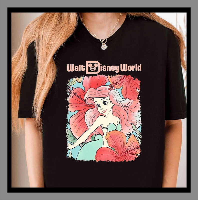 May include: Black t-shirt with a colourful illustration of Ariel from The Little Mermaid, framed by red hibiscus flowers. The text "Walt Disney World" is printed above the illustration in a light pink colour.