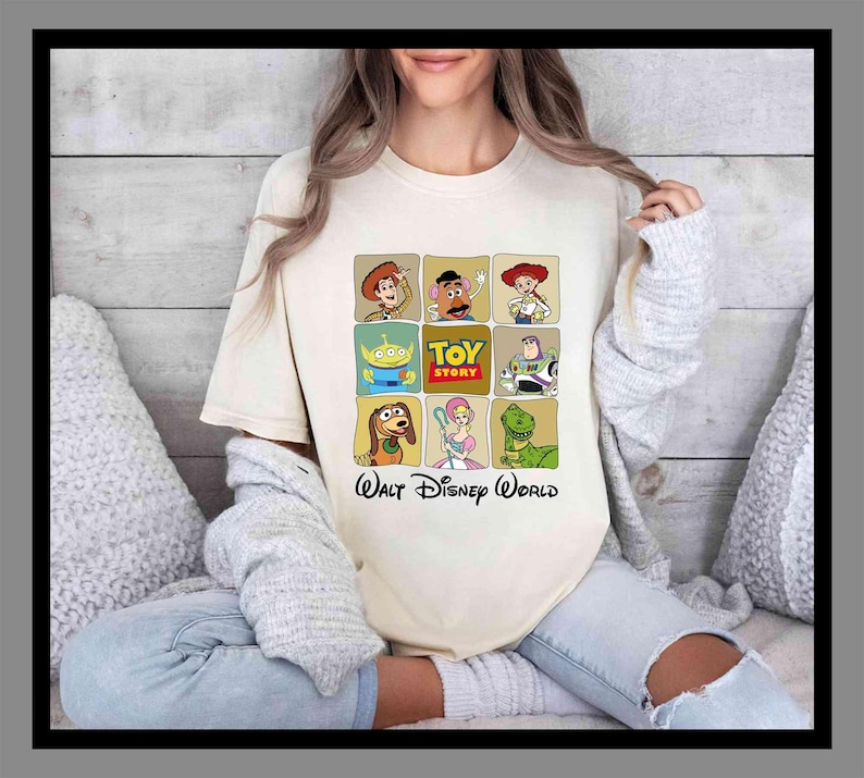 May include: A cream-coloured t-shirt displaying a grid of Toy Story character illustrations. The shirt features Woody, Mr. Potato Head, Jessie, Buzz Lightyear, Slinky Dog, Bo Peep, and Rex. The text "TOY STORY" and "Walt Disney World" are also printed on the shirt.