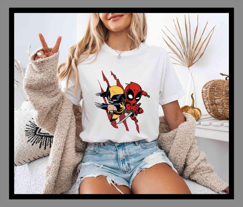 K&ouml;nnte beinhalten: Wei&szlig;es T-Shirt mit einer Cartoon-Grafik von Wolverine und Deadpool. Die Charaktere sind im Chibi-Stil, Wolverine in Gelb und Blau, Deadpool in Rot. Das Design beinhaltet rote Krallen, ein beliebtes Comic-Thema.