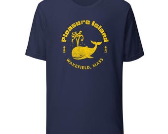 May include: Navy blue t-shirt featuring a yellow graphic of a whale and palm trees inside a circle. The text "Pleasure Island" and "Wakefield, Mass" are also in yellow. A casual tee for everyday wear.