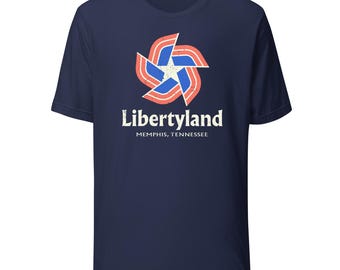 May include: Navy blue t-shirt featuring a retro-style design with a starburst graphic in red, white, and blue. The text "Libertyland" is printed in white, with "Memphis, Tennessee" below it. The shirt is made of a soft material.