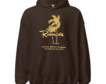 Könnte beinhalten: Ein brauner Kapuzenpullover mit Fronttasche und Kordelzug. Auf der Vorderseite befindet sich eine gelbe Grafik mit Palmen und dem Text "Ramon's Cocoa Beach, Florida, The Toast of the Coast."