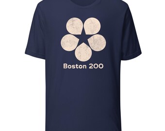 Könnte beinhalten: Marineblaues T-Shirt mit cremefarbenem Blumendesign und einem Stern in der Mitte. Der Text "Boston 200" ist darunter aufgedruckt. Das Shirt hat kurze Ärmel und einen Rundhalsausschnitt.