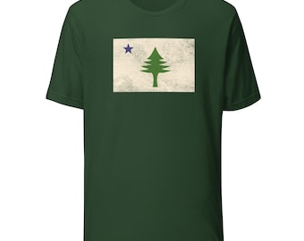 May include: A dark green t-shirt featuring the flag of Maine. The flag design includes a green pine tree and a blue star on a cream-colored background. The shirt is made of a soft material.