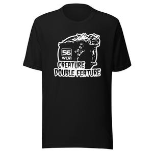 May include: Black t-shirt featuring a white graphic of a monster and the text "56 WLVI CREATURE DOUBLE FEATURE". The design includes a stylized creature with sharp teeth and claws.