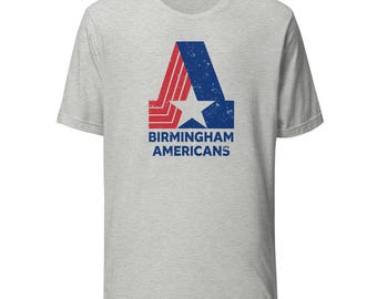 Könnte beinhalten: Ein hellgraues T-Shirt mit einem verwitterten Logo der Birmingham Americans. Das Logo zeigt ein blau-rotes Design mit einem weißen Stern und den Worten "BIRMINGHAM AMERICANS" in Blau.