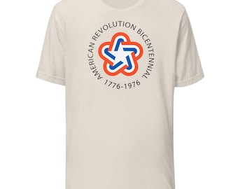 May include: A cream-colored t-shirt featuring a circular graphic with the text "American Revolution Bicentennial 1776-1976." The graphic includes a star-shaped design in red, white, and blue.