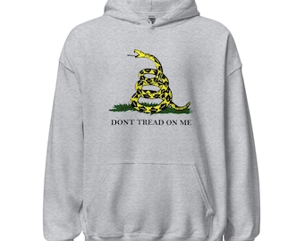 May include: A light gray hooded sweatshirt featuring a yellow and black coiled snake on green grass. The text "DON'T TREAD ON ME" is printed below the snake graphic. The hoodie has a front pocket and a drawstring hood.