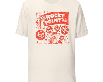 May include: A cream-colored short-sleeve t-shirt featuring a red graphic print that reads Rocky Point Park, Warwick, Rhode Island, Fun, Prizes, Thrills, and Rides. The design includes illustrations of a lobster and two children waving.
