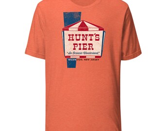 May include: Orange t-shirt featuring a vintage-style graphic for Hunt's Pier, with a red and white striped tent design and the text "An Oceanic Wonderland." The shirt also includes the text "Wildwood, New Jersey."