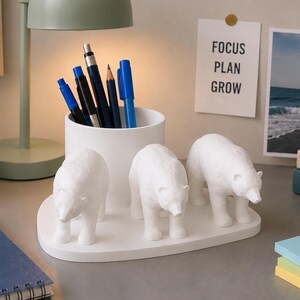May include: A white desk organizer with three polar bear figurines. A white pen holder with pens and pencils, a notebook with the text "EXPLORE MORE", and a small potted plant are also on the desk.