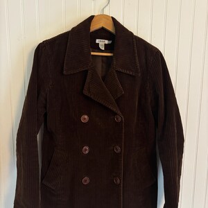 May include: A brown corduroy jacket with a double-breasted design. The jacket has a notched collar, two front pockets, and four brown buttons. The brand "IZOD" is visible on the label.