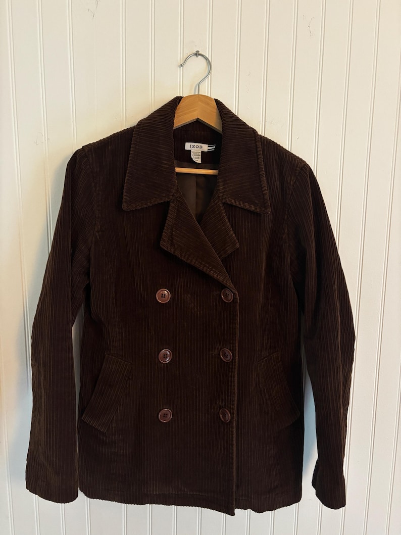 May include: A brown corduroy jacket with a double-breasted design. The jacket has a notched collar, two front pockets, and four brown buttons. The brand "IZOD" is visible on the label.