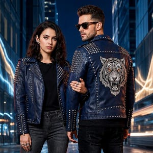 Puede incluir: Dos chaquetas de cuero azul oscuro con tachuelas metálicas plateadas en solapas, hombros y mangas. La espalda de una chaqueta muestra un gráfico bordado detallado de una cabeza de tigre con ojos naranjas, ambas tienen cuello estructurado.