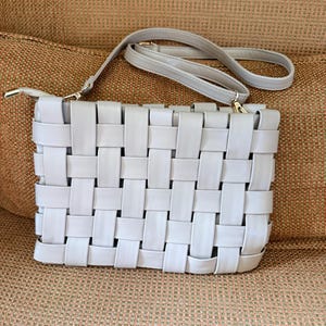 Pu&ograve; includere: Una pochette intrecciata grigio chiaro con una tracolla abbinata. La borsa rettangolare presenta un design a trama a cestino e hardware color oro. La tracolla &egrave; regolabile e staccabile.