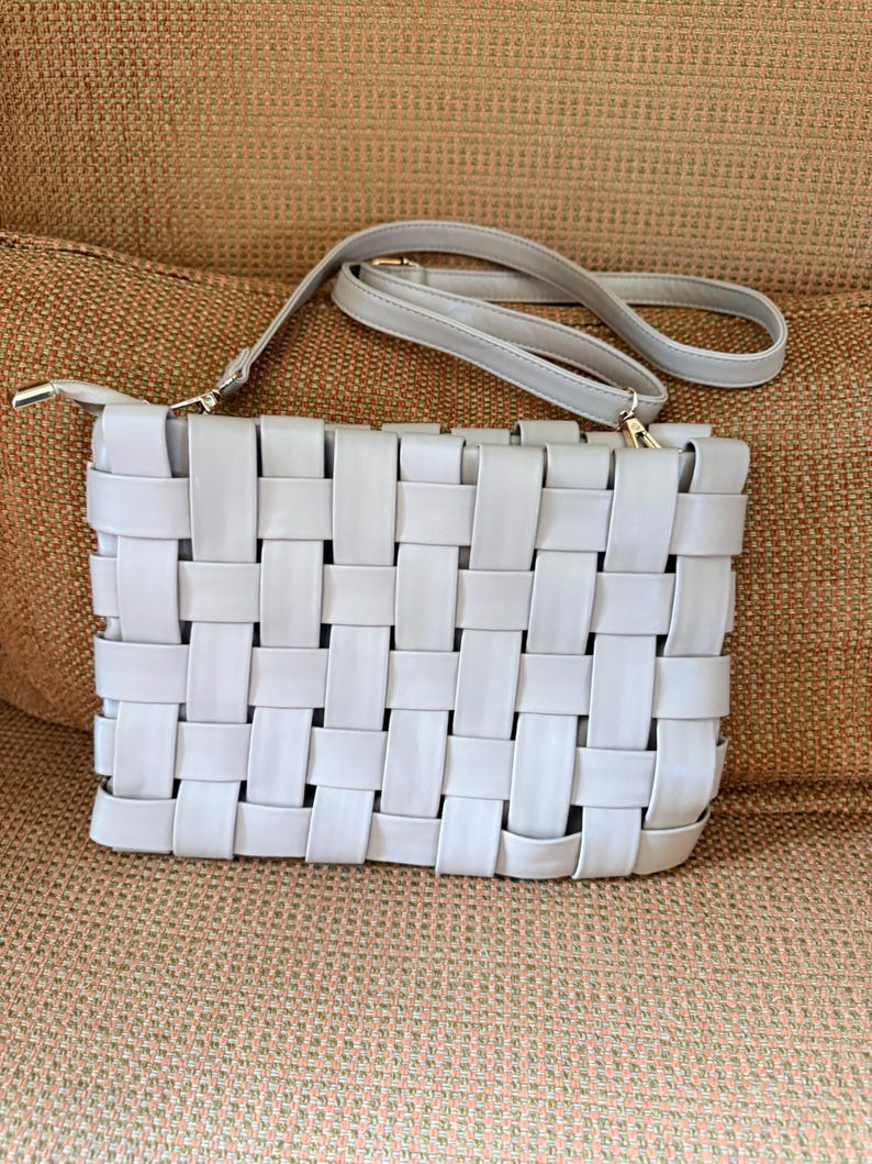Pu&ograve; includere: Una pochette intrecciata grigio chiaro con una tracolla abbinata. La borsa rettangolare presenta un design a trama a cestino e hardware color oro. La tracolla &egrave; regolabile e staccabile.