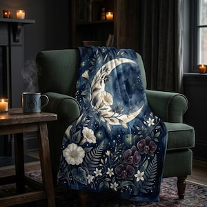 May include: A dark blue throw blanket featuring a large cream-colored crescent moon surrounded by white morning glory flowers, dark purple orchids, green fern leaves, and small glowing stars against a deep navy watercolor-style background.