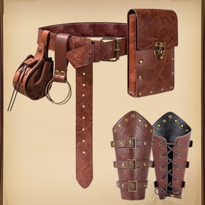 K&ouml;nnte beinhalten: Ein brauner Lederg&uuml;rtel mit einer Tasche, einem rechteckigen Etui und zwei Armsch&uuml;tzern. Der G&uuml;rtel hat eine Schnalle und L&ouml;cher zur Verstellung. Die Tasche und das Etui haben dekorative Nieten. Die Armsch&uuml;tzer haben Schnallen und Riemen.