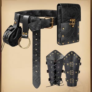 K&ouml;nnte beinhalten: Schwarzes Lederg&uuml;rtel-Set mit einer Tasche, einer Handytasche und zwei Armsch&uuml;tzern. Der G&uuml;rtel hat eine Schnalle und einen dekorativen Riemen. Die Tasche ist klein und rund, und die Handytasche hat einen Verschluss.